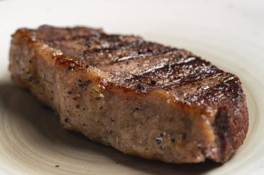 Mavi ahşap arka planda beyaz tabakta baharatlı ızgara biftek.