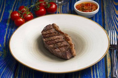 Kızarmış biftek, kiraz domatesleri, mavi ahşap masada tuz ve biber..