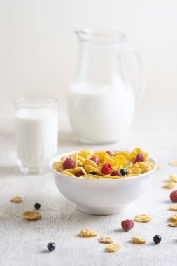 Beyaz arka planda ahududu ve yaban mersinli mısır gevreği. Kahvaltı. Böğürtlenli ve sütlü mısır gevreği. Mısır gevreği. Taze sağlıklı yiyecekler. Sabah yemeği. Tahta masa. Organik. Diyet kavramı.