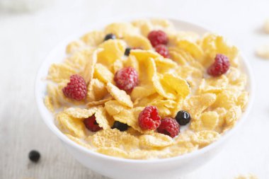 Mısır gevreği, yabanmersini ve ahududu ile sağlıklı kahvaltı. Sağlıklı mısır gevreği, süt ve böğürtlenli kase. Meyveli leziz yuvarlak mısır gevreği. Diyet konsepti. Kapat.