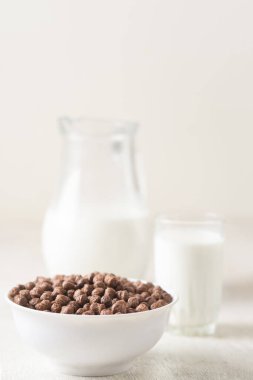 Beyaz ahşap arka planda çikolatalı mısır topu ve süt dolu bir kase..