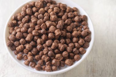 Beyaz ahşap arka planda çikolatalı mısır topu ve süt dolu bir kase..