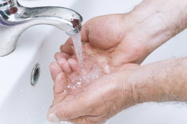 Yaşlı adam ellerini banyoda yıkar. Corona virüsü sık sık ellerini temizleyerek salgına karşı korur..