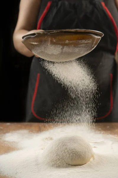 Baker pours flour for making pizza. Chef cooking dough to bake a cake on a wooden table. The process of making home baking. Cooking pasta, bread,spaghetti,khachapuri, food concept