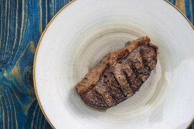 Mavi ahşap arka planda beyaz tabakta baharatlı ızgara biftek.