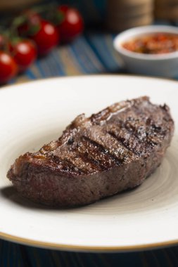 Kızarmış biftek, kiraz domatesleri, mavi ahşap masada tuz ve biber..