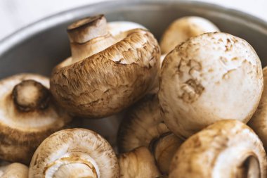 Beyaz ahşap arka planda demir bir kasede çiğ mantar.