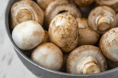 Beyaz ahşap arka planda demir bir kasede çiğ mantar.