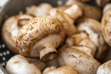 Beyaz ahşap arka planda demir bir kasede çiğ mantar.