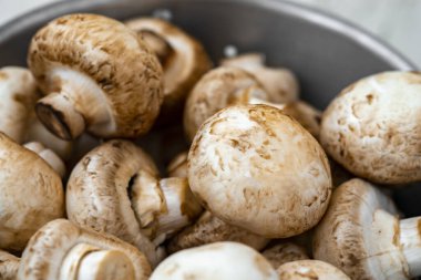 Beyaz ahşap arka planda demir bir kasede çiğ mantar.