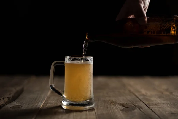male hand pouring beer from bottle into glass on black background
