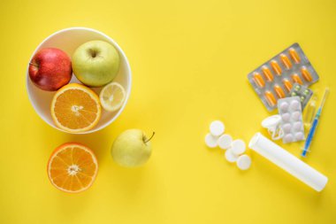 Tabaktaki meyvelerin ve ilaçların üst görüntüsü, sentetik vitaminlere karşı meyve seçimi kavramı.