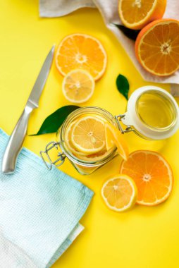 Cam kavanozda dilimlenmiş limon ve portakal manzarası ve sarı arka planda ev yapımı koruma kavramı.