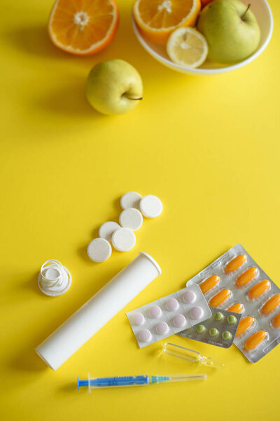 Вид сверху на лекарство на желтом фоне с тарелкой фруктов рядом
