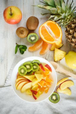Beyaz bir tabakta meyve dilimlerinin üst görüntüsü ve parlak ahşap arka planda farklı meyvelerle dolu ahşap bir kaşık.