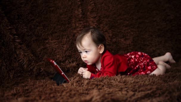 Baby flicka håller en tablett och sitter på golvet — Stockvideo