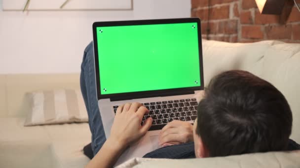 Personen ved bordet leser Internett på en grønn laptop-skjerm. I en godt opplyst, koselig leilighet. En mann jobber i – stockvideo