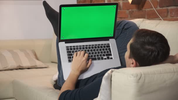 La personne à la table navigue sur Internet sur un écran d'ordinateur portable vert. Dans un appartement bien éclairé et confortable. Un homme travaille dans — Video