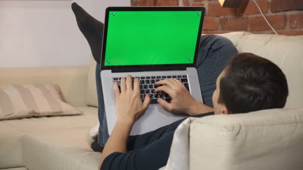 Osoba u stolu si prohlíží internet na zelené obrazovce notebooku. V dobře osvětleném, útulném bytě. Muž tam pracuje. — Stock video
