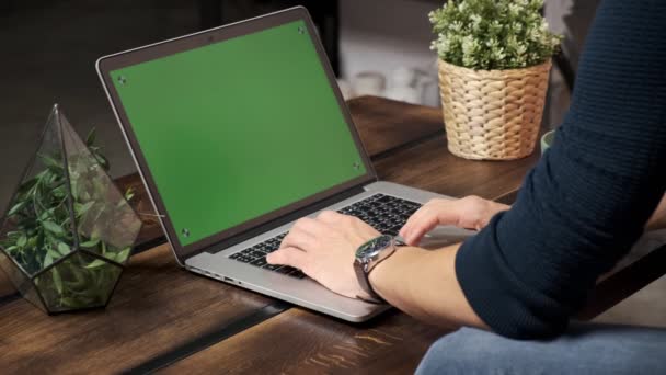 Людина за столом переглядає Інтернет на зеленому екрані ноутбука. У добре освітленій, затишній квартирі. Людина працює в — стокове відео