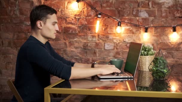 Человек за столом просматривает Интернет на зеленом экране ноутбука. В хорошо освещенной, уютной квартире. Мужчина работает в — стоковое видео