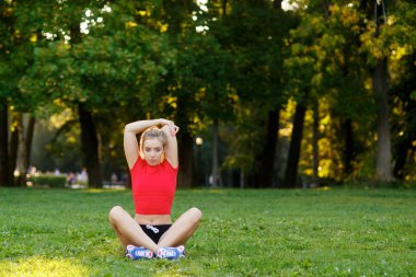 Genç ve güzel bir kadın parkta çimlerin üzerinde yoga yapıyor. Antrenman ve esneme kasları