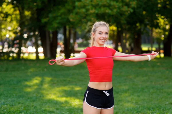 Młoda kobieta trenuje z gumkami na zewnątrz. Koncepcja zdrowego stylu życia. dziewczyna robi fitness w parku na łonie natury — Zdjęcie stockowe