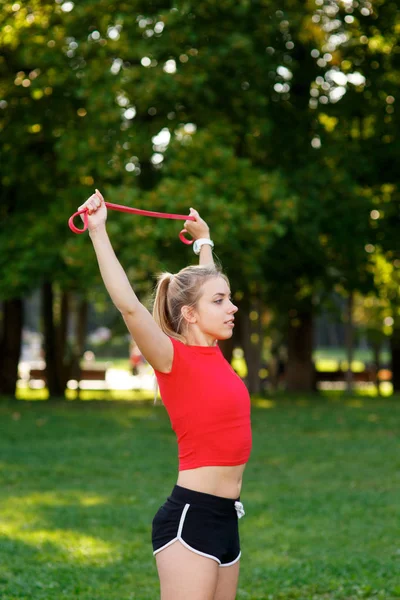Mujer joven está entrenando con bandas de goma al aire libre. Concepto de estilo de vida activo saludable. chica haciendo fitness en el parque en la naturaleza —  Fotos de Stock