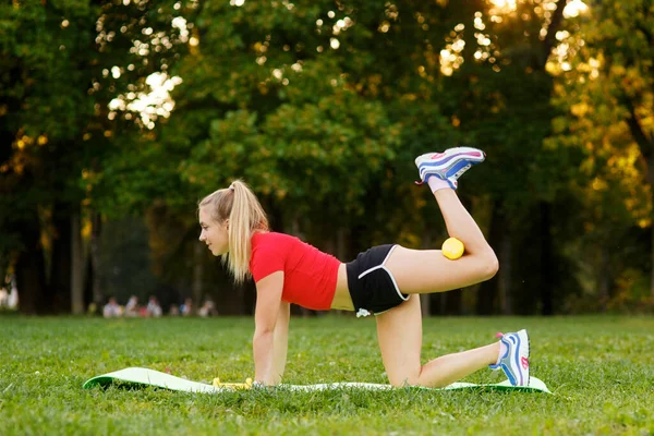 Egészséges, fiatal, sportos nő, aki négykézláb gyakorolja a gyakorlatokat, kiegyenesítve a lábát a szabadban. Koncepció sport, fitness, életmód. — Stock Fotó