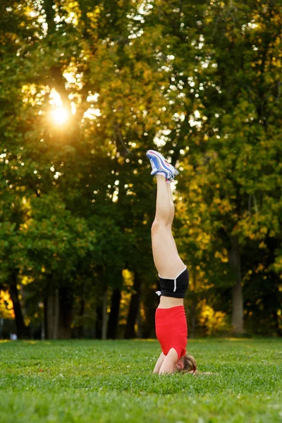 Uma jovem pratica ioga na natureza. mulher executa um headstand em um parque. Conceito - estilo de vida saudável e ativo. — Fotografia de Stock