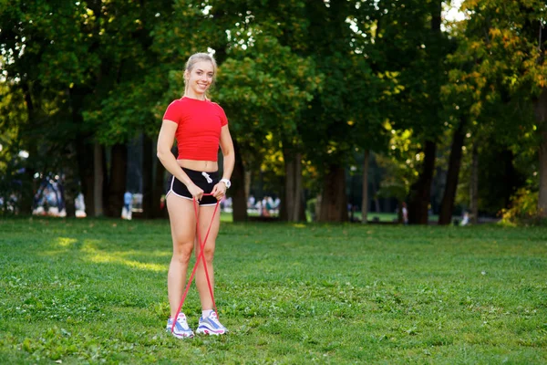 Giovane donna si allena con elastici all'aperto. Sano concetto di stile di vita attivo. ragazza che fa fitness nel parco sulla natura — Foto Stock