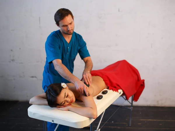 Junge Asiatin genießt die therapeutische Wirkung einer traditionellen Hot-Stone-Massage im luxuriösen Spa- und Wellnesszentrum — Stockfoto