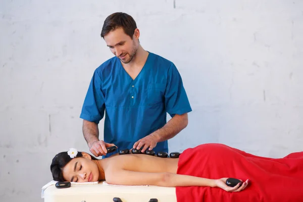 Ung asiatisk kvinna njuter av de terapeutiska effekterna av en traditionell hot stone massage på lyx spa och wellness center — Stockfoto