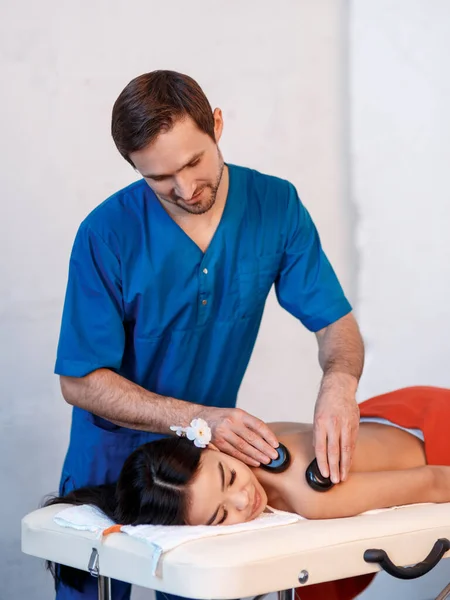 Mujer joven asiática que disfruta de los efectos terapéuticos de un masaje tradicional de piedra caliente en el lujoso spa y centro de bienestar. — Foto de Stock