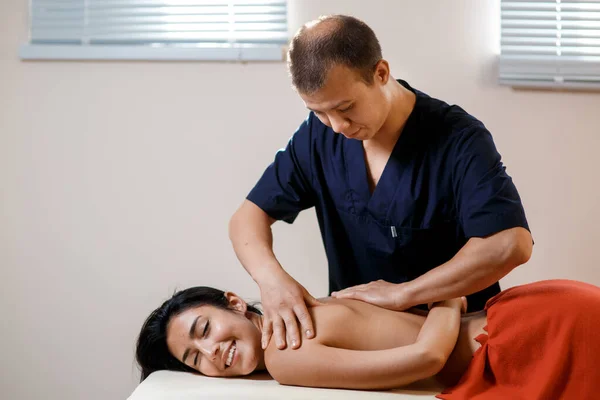 En ung kvinna får en massagebehandling. Masseur gör tillbaka massage. — Stockfoto