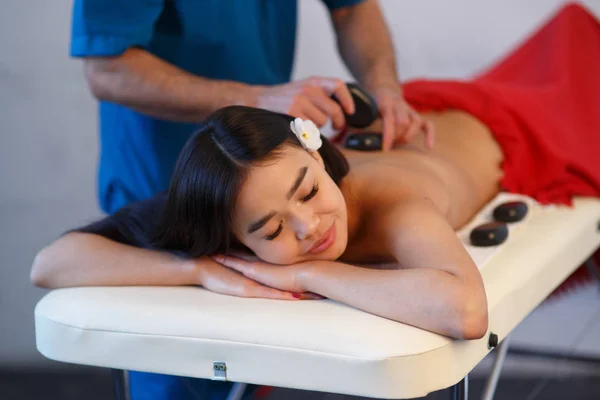 Mujer tumbada en la mesa de masajes con piedras en la espalda en el spa —  Fotos de Stock