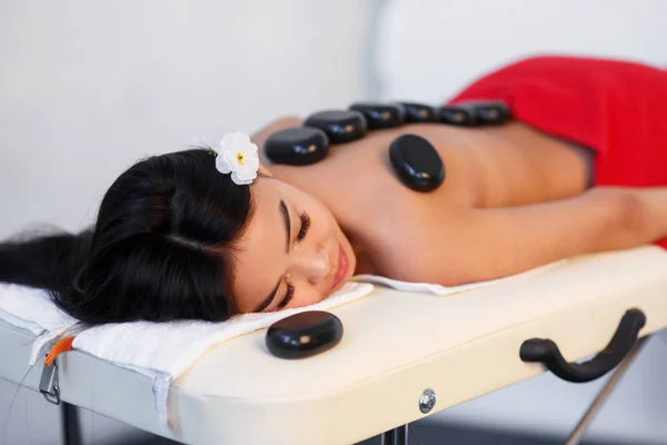 Woman lying on massage table with stones on her back at spa — Stock Photo, Image