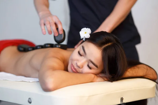 Giovane donna asiatica godendo gli effetti terapeutici di un massaggio tradizionale hot stone presso spa di lusso e centro benessere — Foto Stock