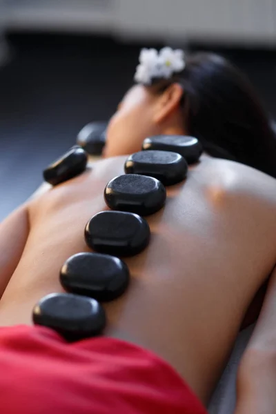 Woman lying on massage table with stones on her back at spa — Stock Photo, Image