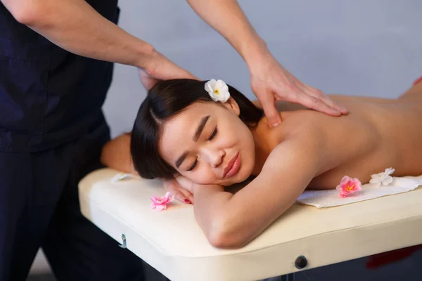 Male masseur does a back massage to a girl of Asian appearance. Relaxing and tonic massage. — Stock Photo, Image