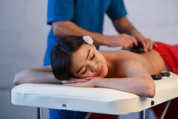 Ung asiatisk kvinna njuter av de terapeutiska effekterna av en traditionell hot stone massage på lyx spa och wellness center — Stockfoto