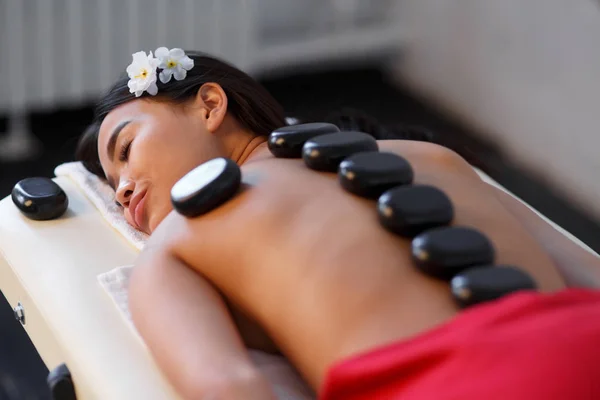 Donna sdraiata sul tavolo da massaggio con pietre sulla schiena al centro benessere — Foto Stock