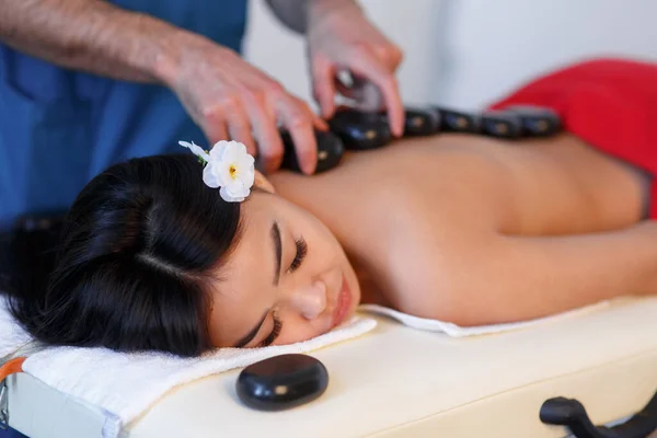 Jovem asiática desfrutando dos efeitos terapêuticos de uma massagem tradicional em pedra quente no spa de luxo e centro de bem-estar — Fotografia de Stock