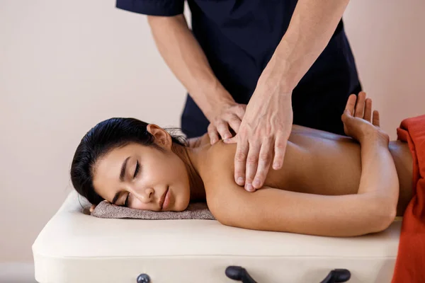 Eine junge Frau bekommt einen Massagevorgang. Masseur Marken Rücken Massage. — Stockfoto