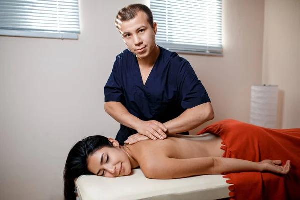 Eine junge Frau bekommt einen Massagevorgang. Masseur Marken Rücken Massage. — Stockfoto
