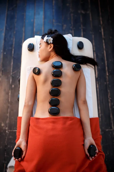 Mujer tumbada en la mesa de masajes con piedras en la espalda en el spa —  Fotos de Stock