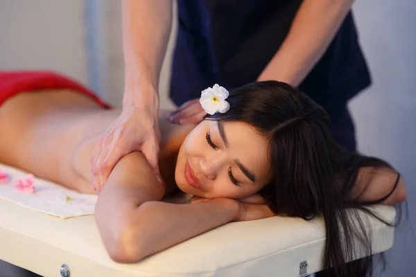 Massagista masculino faz uma massagem nas costas para uma menina de aparência asiática. Massagem relaxante e tônica . — Fotografia de Stock