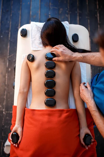 Mujer tumbada en la mesa de masajes con piedras en la espalda en el spa —  Fotos de Stock