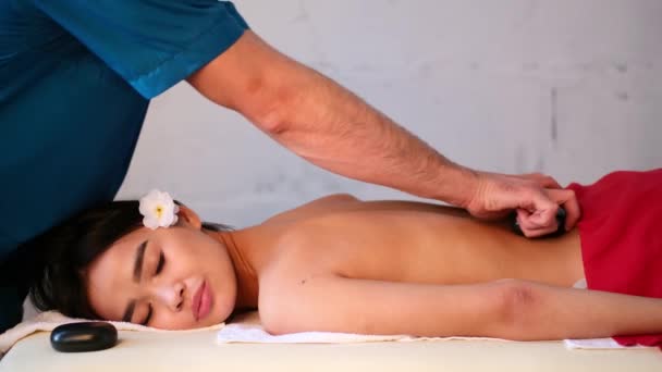 Мужской массажист делает массаж спины девушке азиатской внешности. расслабляющий и тонизирующий массаж . — стоковое видео