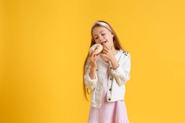 Doğum günü şapkalı, gülümseyen, eğlenen ve gözlerindeki iki kırmızı çöreğe bakan çılgın sarışın kız. Şekerler. Sarı stüdyo arka planı.